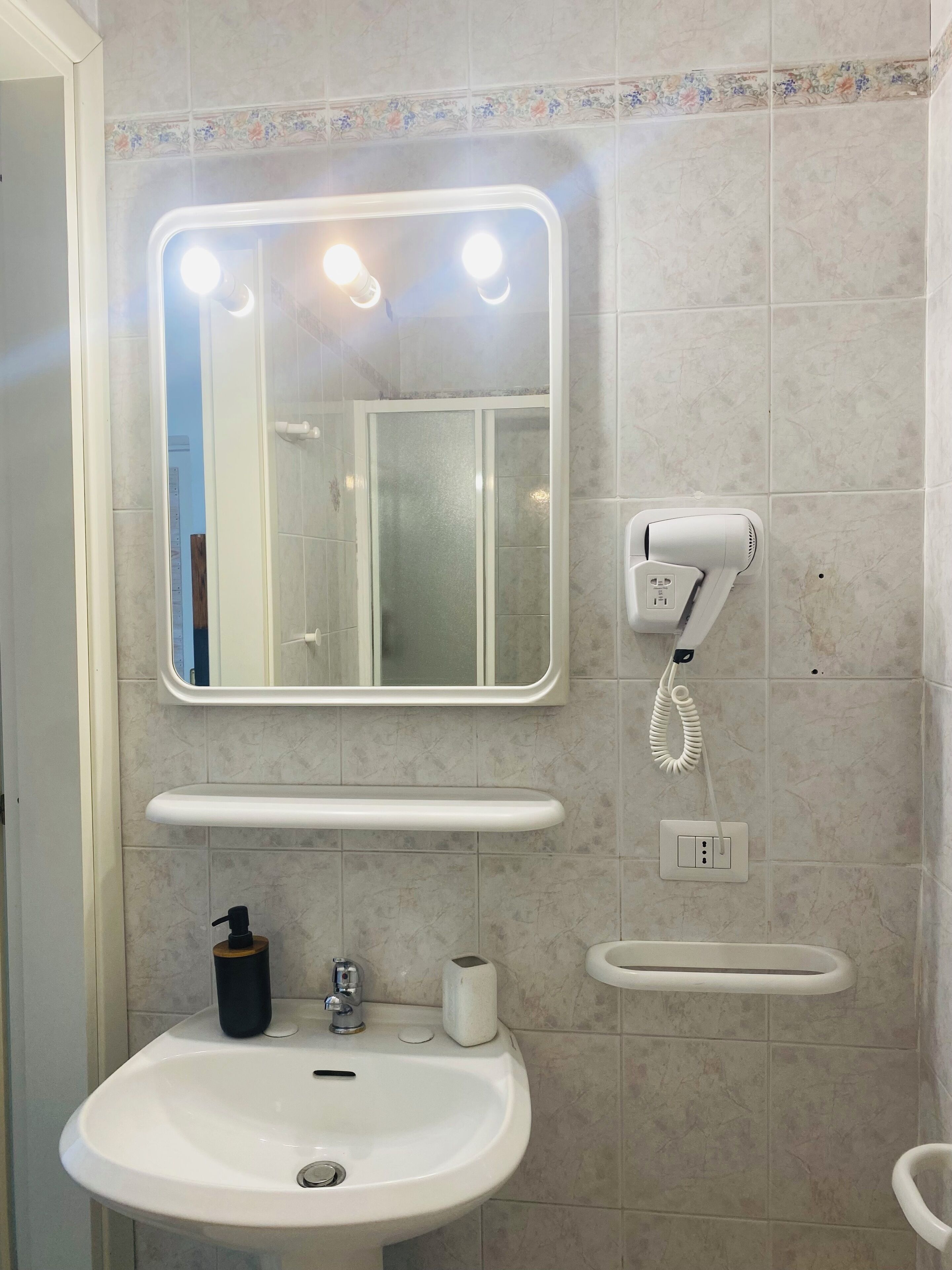 A bathroom with a white sink, a mirror with lights, a hairdryer, and a toilet.
