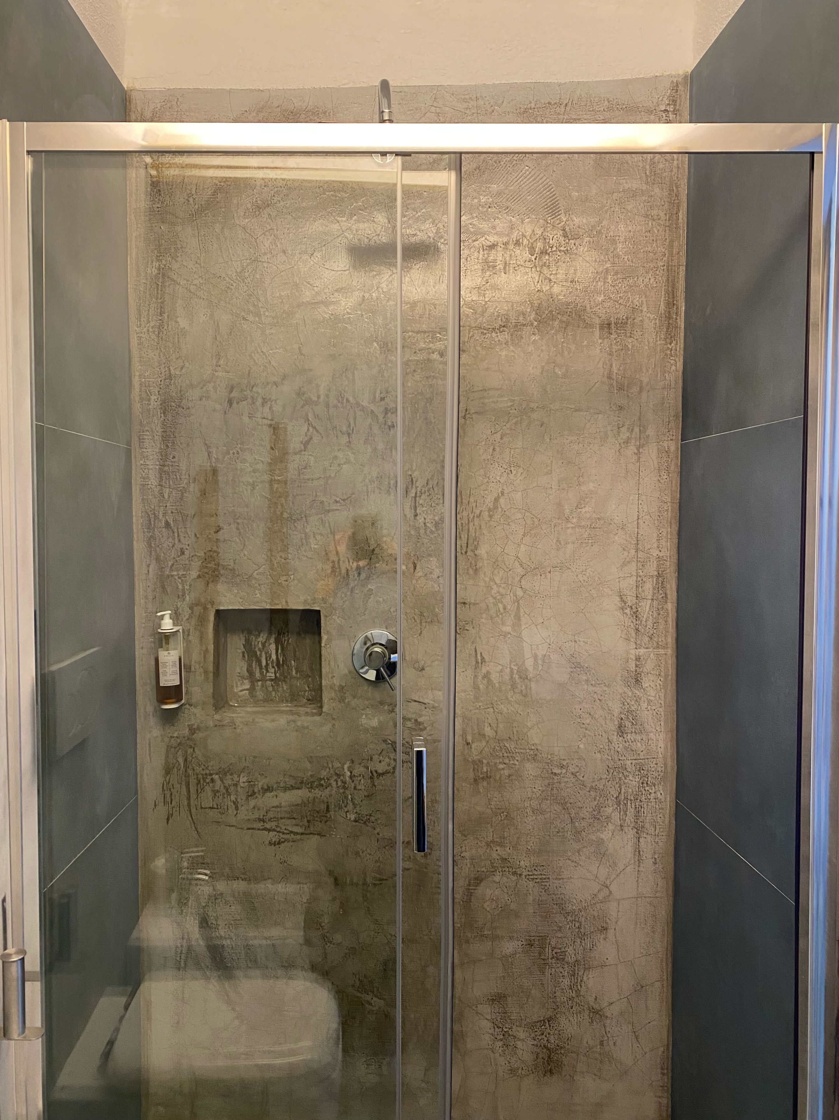 A walk-in shower with a glass door, a built-in bench, and a handheld showerhead.
