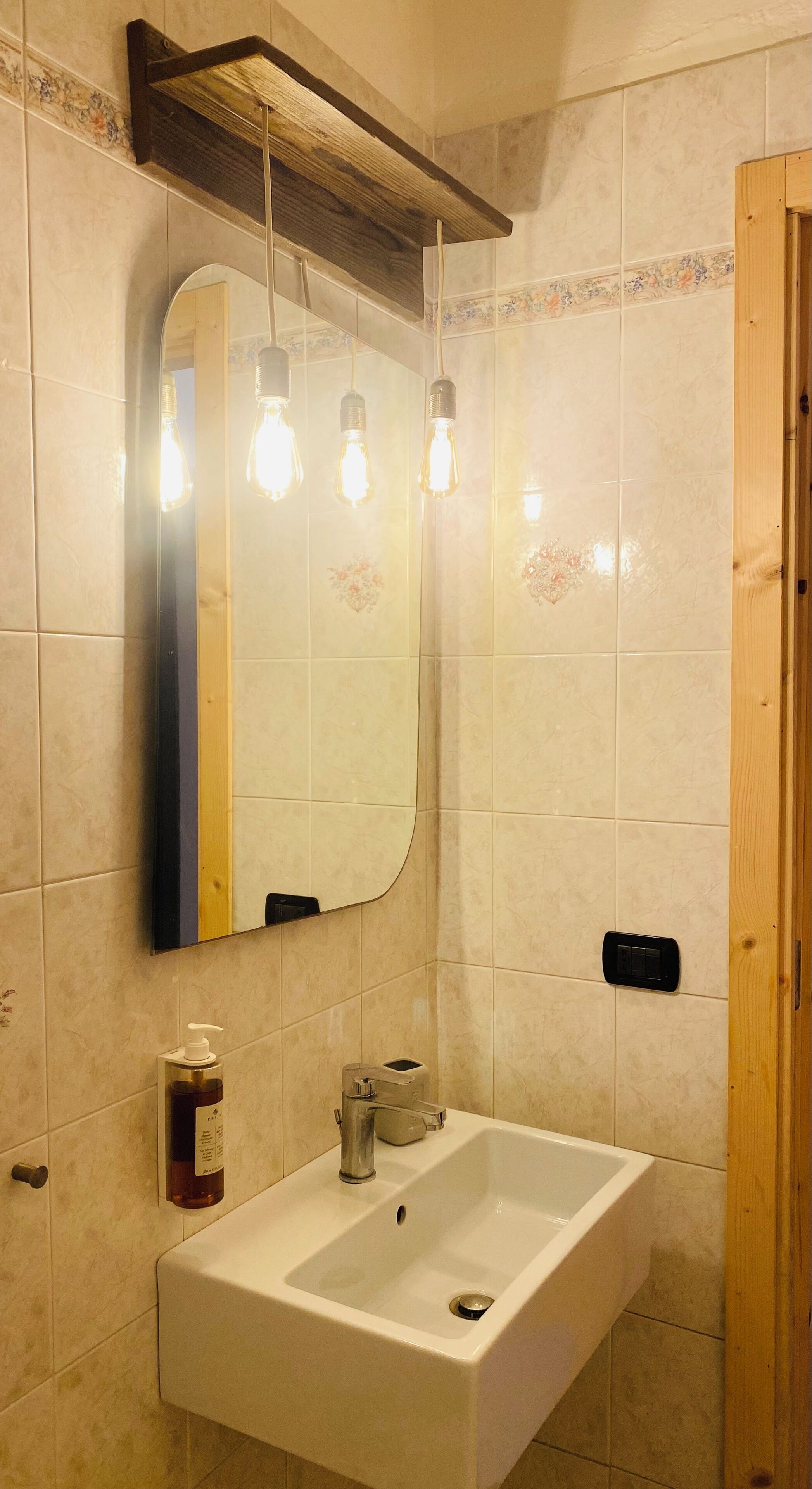A bathroom with a rectangular sink, a mirror, and three hanging light bulbs.