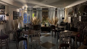 Uma sala de jantar com balcão, mesas, cadeiras e uma parede de pedra com espelho.