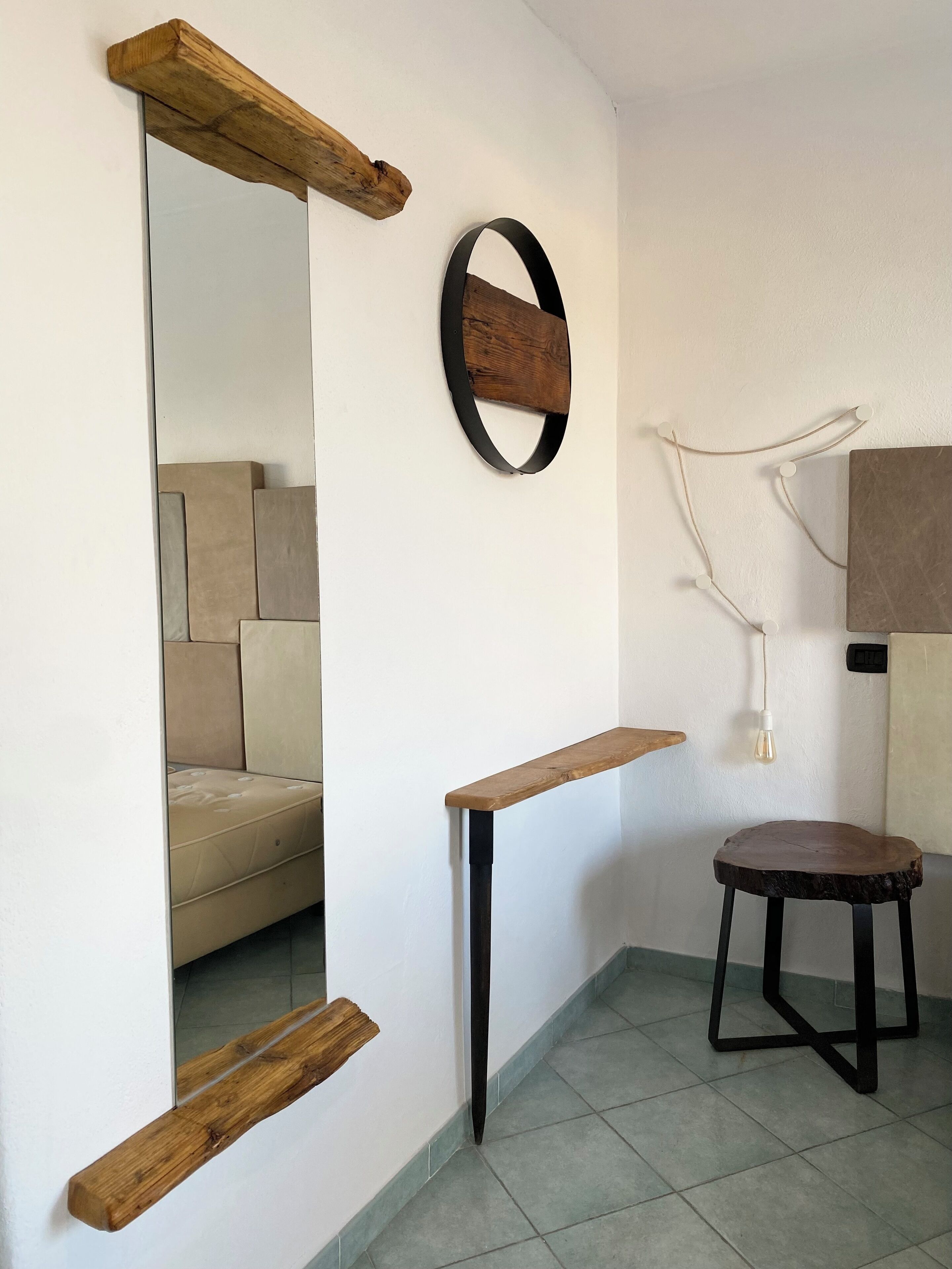 Une pièce avec un miroir, une étagère en bois, un petit tabouret et un luminaire fixé au mur.