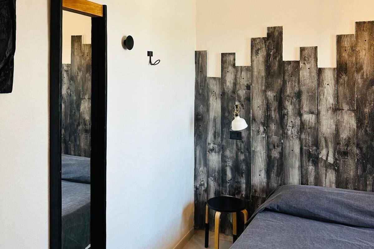 A bedroom with a bed, a mirror, a small table, and a wall-mounted lamp.
