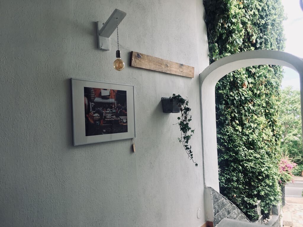 A wall with a framed picture, a wooden plank, a hanging light fixture, and a potted plant.