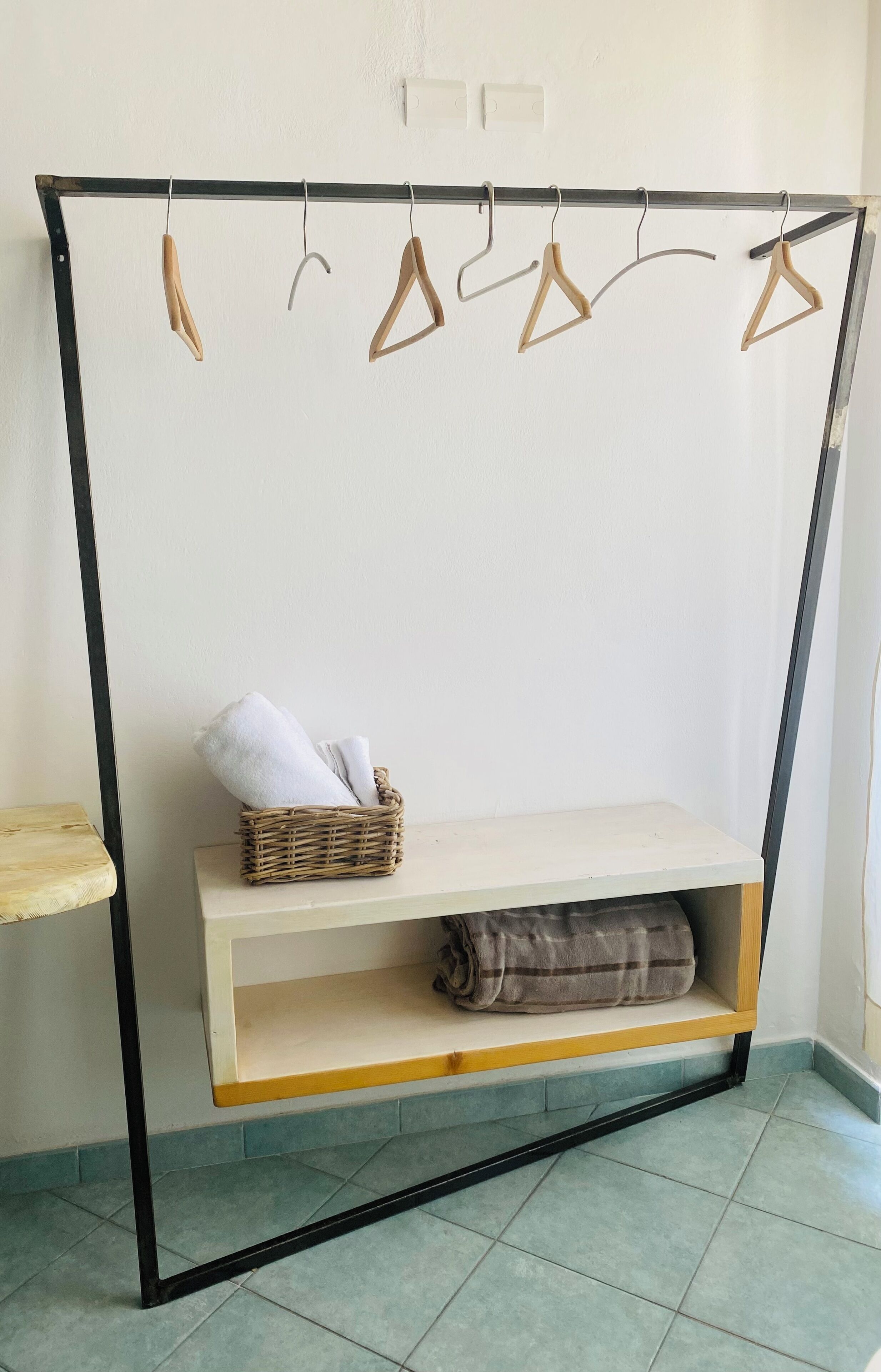 A wardrobe with a shelf and hanging space, a wicker basket with towels, and a tiled floor.