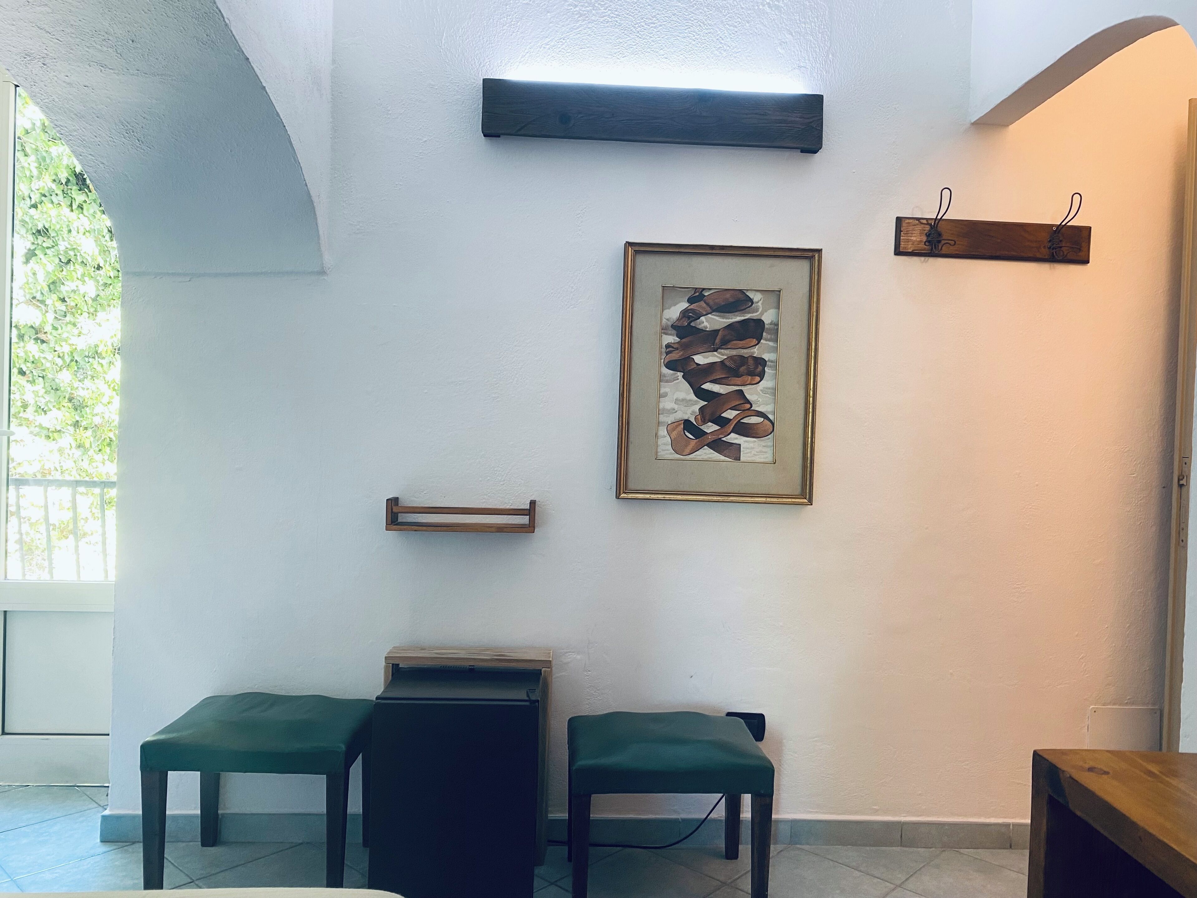 Een kamer met een witte muur, een lijstwerk, een houten plank en twee groene zitbankjes.