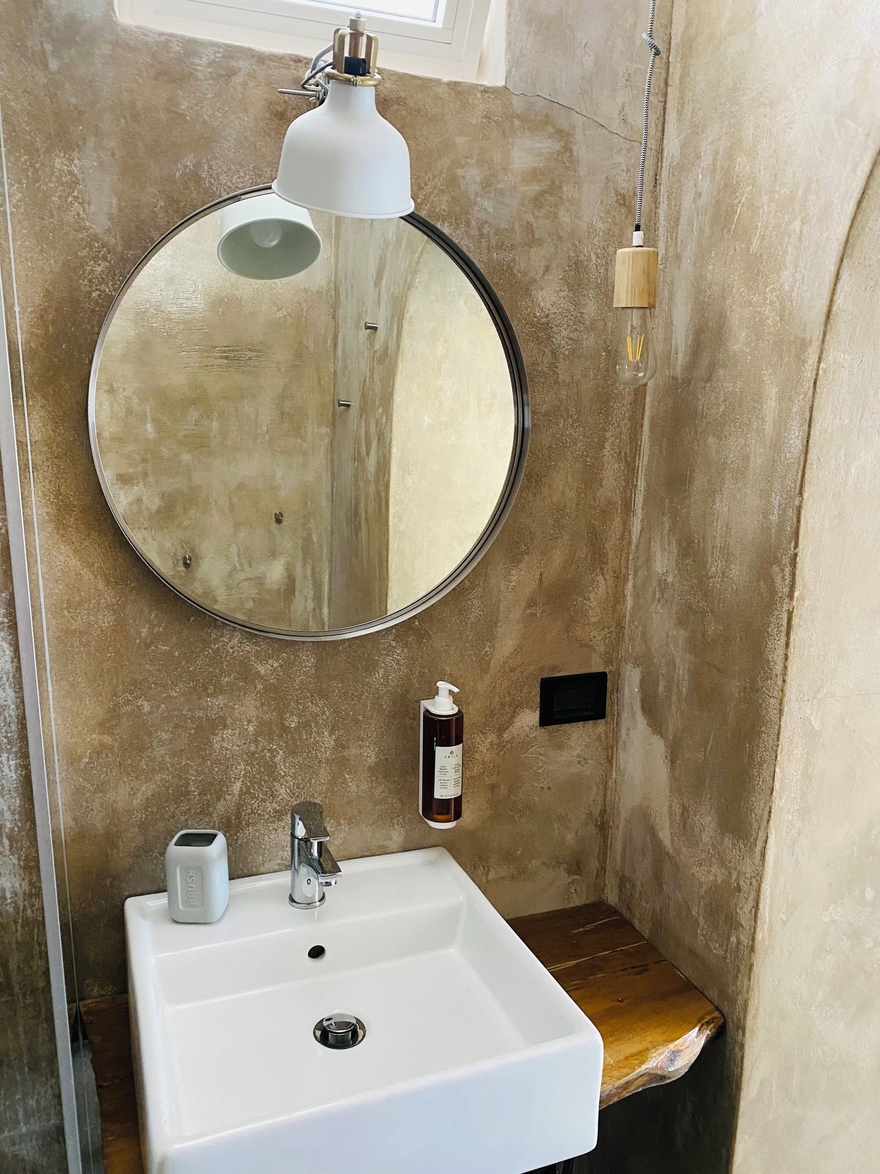 A bathroom with a round mirror, a white sink, a soap dispenser, and a towel rack.