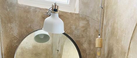 A bathroom with a round mirror, a white sink, a soap dispenser, and a towel rack.
