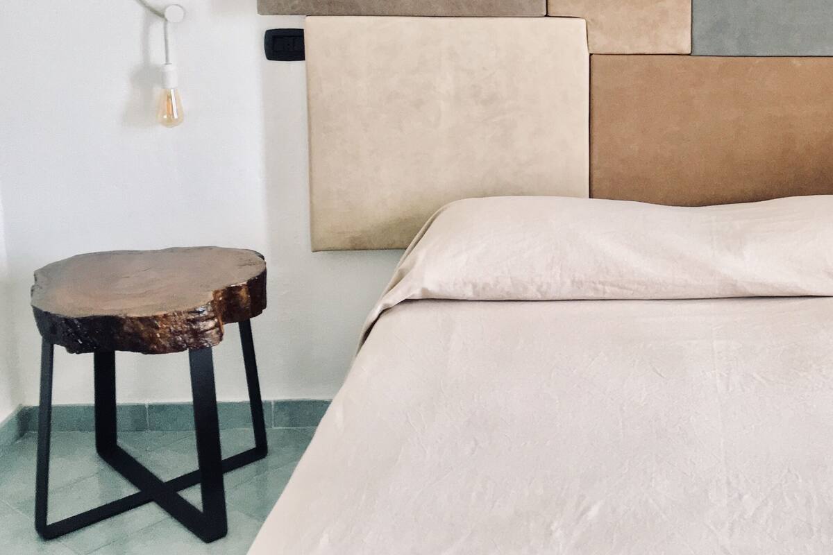 A bedroom with a bed, a nightstand, and a wall-mounted lamp.