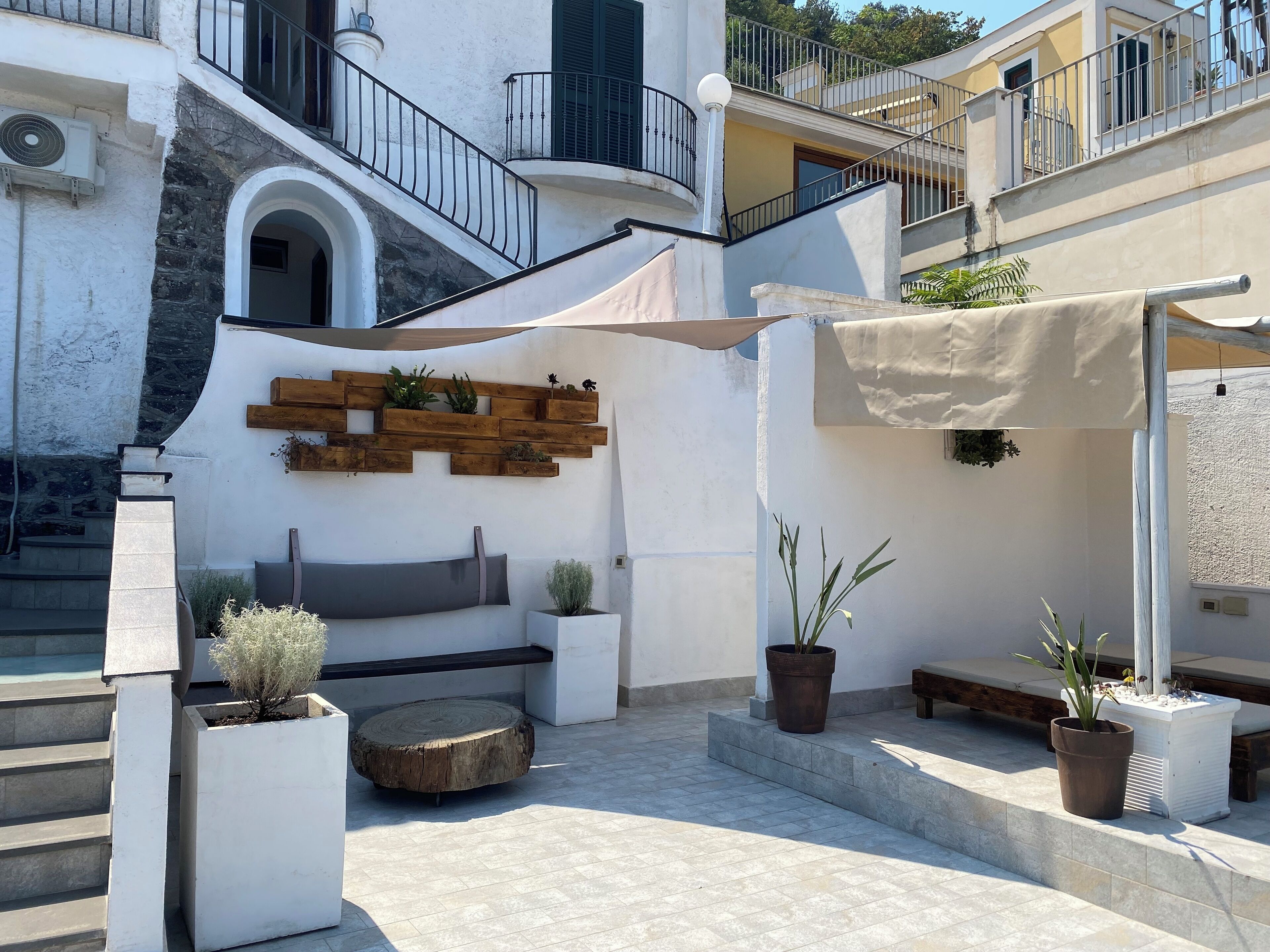 Une cour avec un banc en pierre, des plantes en pot et un mur décoratif fait de jardinières en bois.