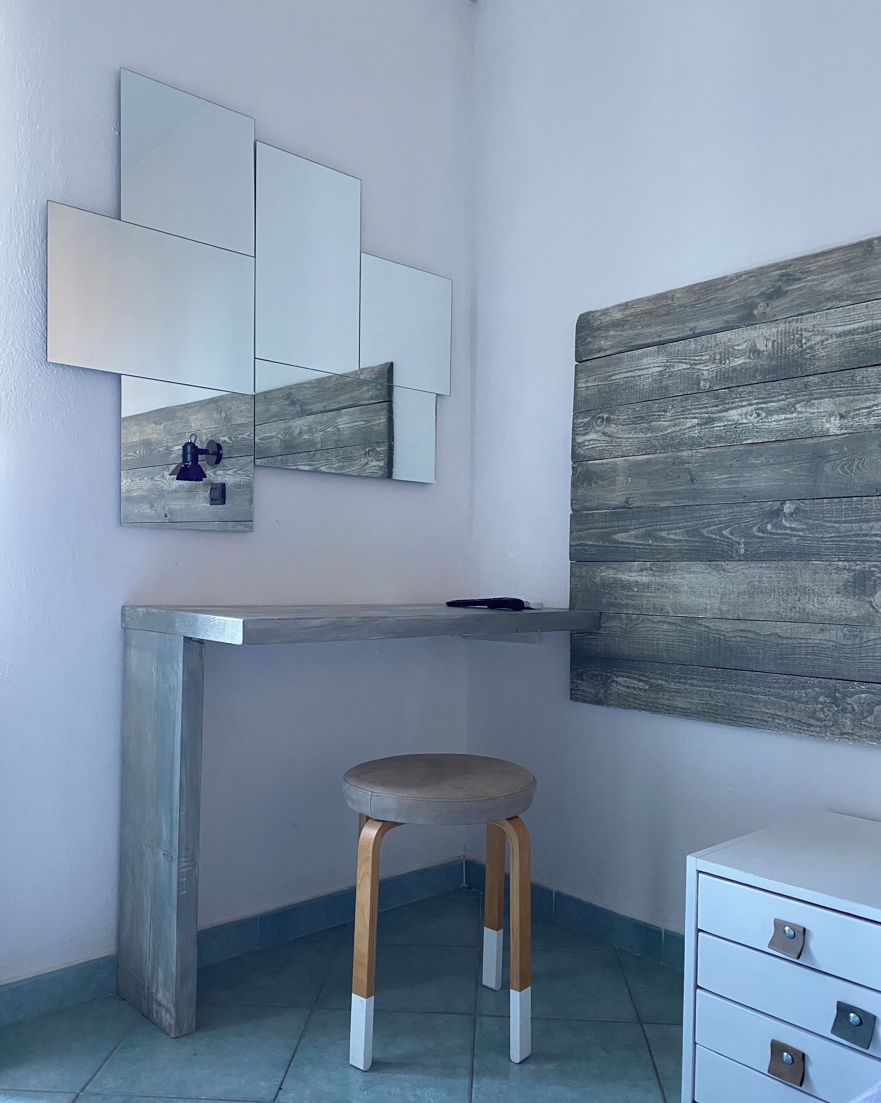 A modern bathroom with a concrete bench, a wooden stool, a mirror, and a wooden wall panel.
