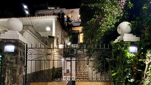 Uma entrada com portão e um caminho de azulejos que leva a um edifício com varanda.