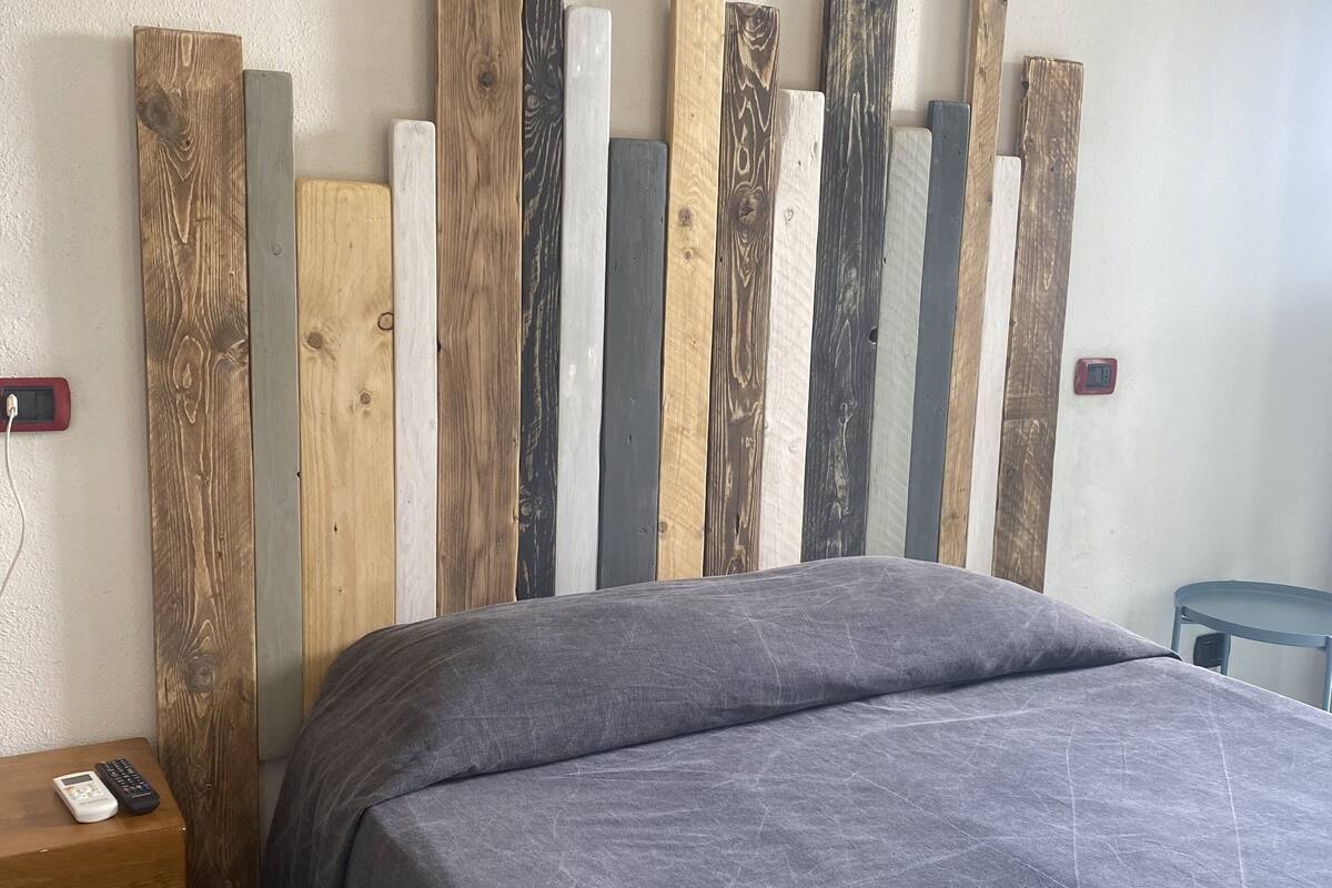 A bedroom with a bed, a nightstand, and a wall-mounted thermostat.