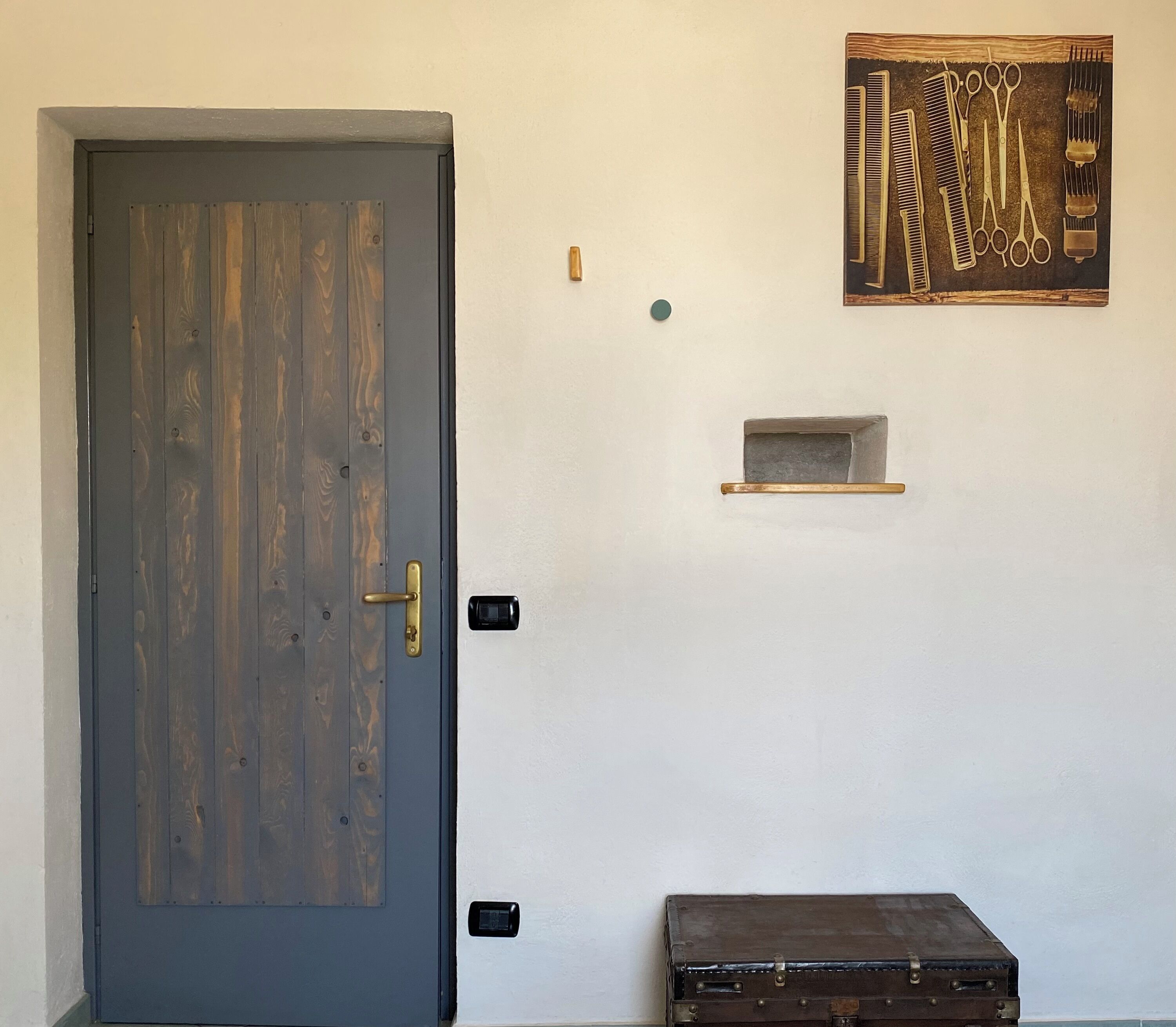 A wooden door with a brass handle, a small shelf with grooming tools, and a vintage suitcase against a white wall.