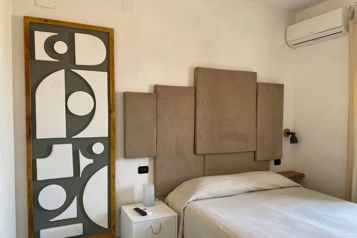 A bedroom with a bed, a nightstand, a wall-mounted air conditioner, and a decorative panel.