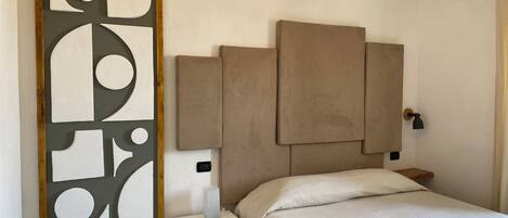 A bedroom with a bed, a nightstand, a wall-mounted air conditioner, and a decorative panel.