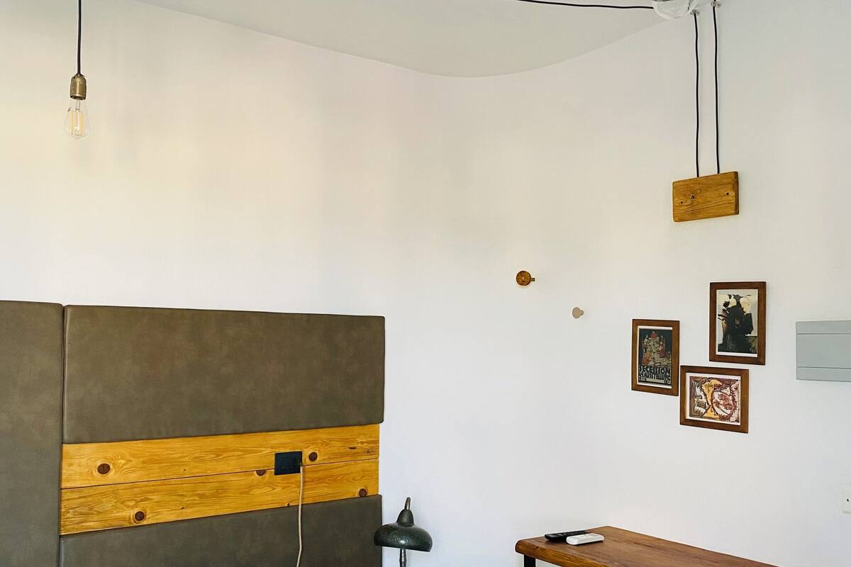 A bedroom with a bed, a desk, a stool, and a hanging light fixture.