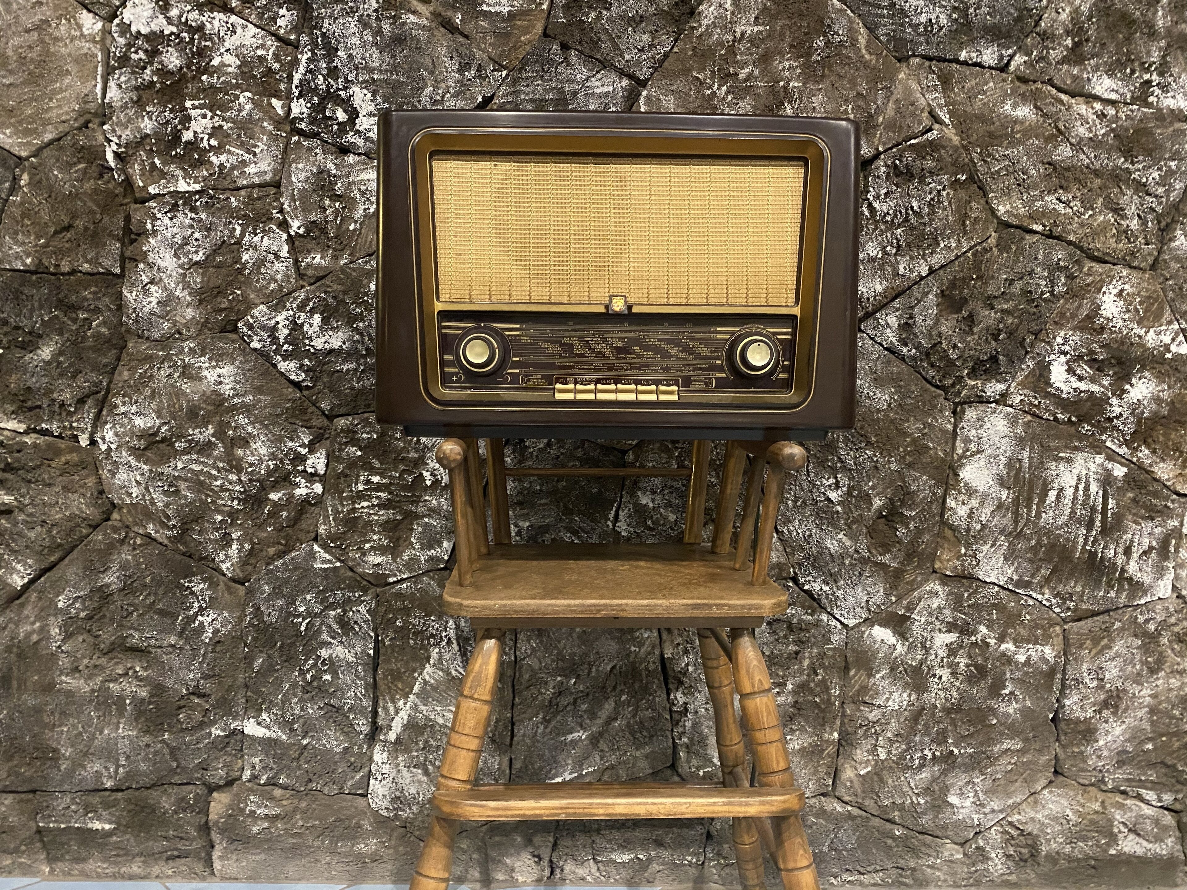 A vintage radio on a wooden stand against a textured stone wall.