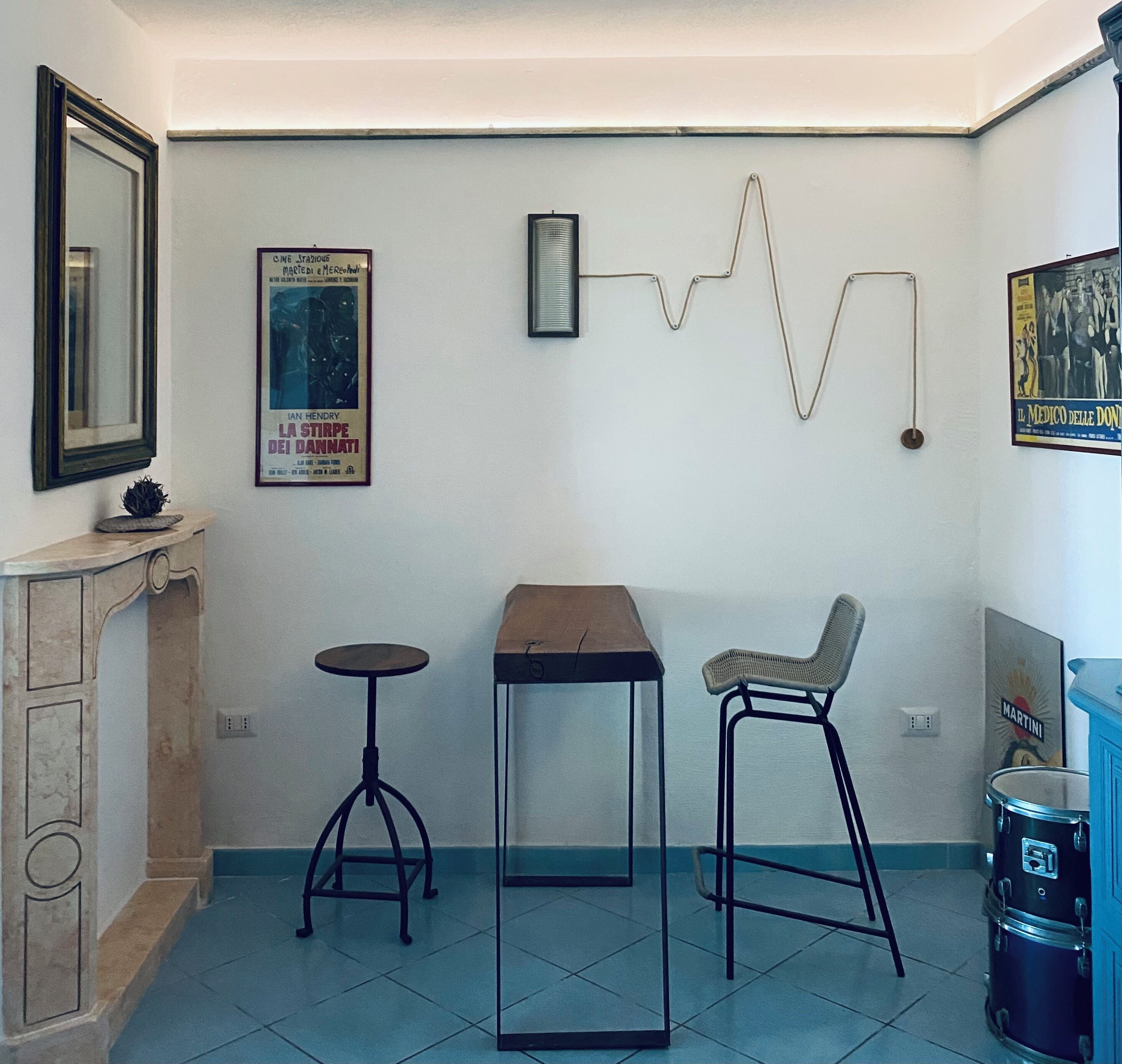 A room with a tiled floor, a wooden table, two stools, a mirror, and wall decorations including movie posters.