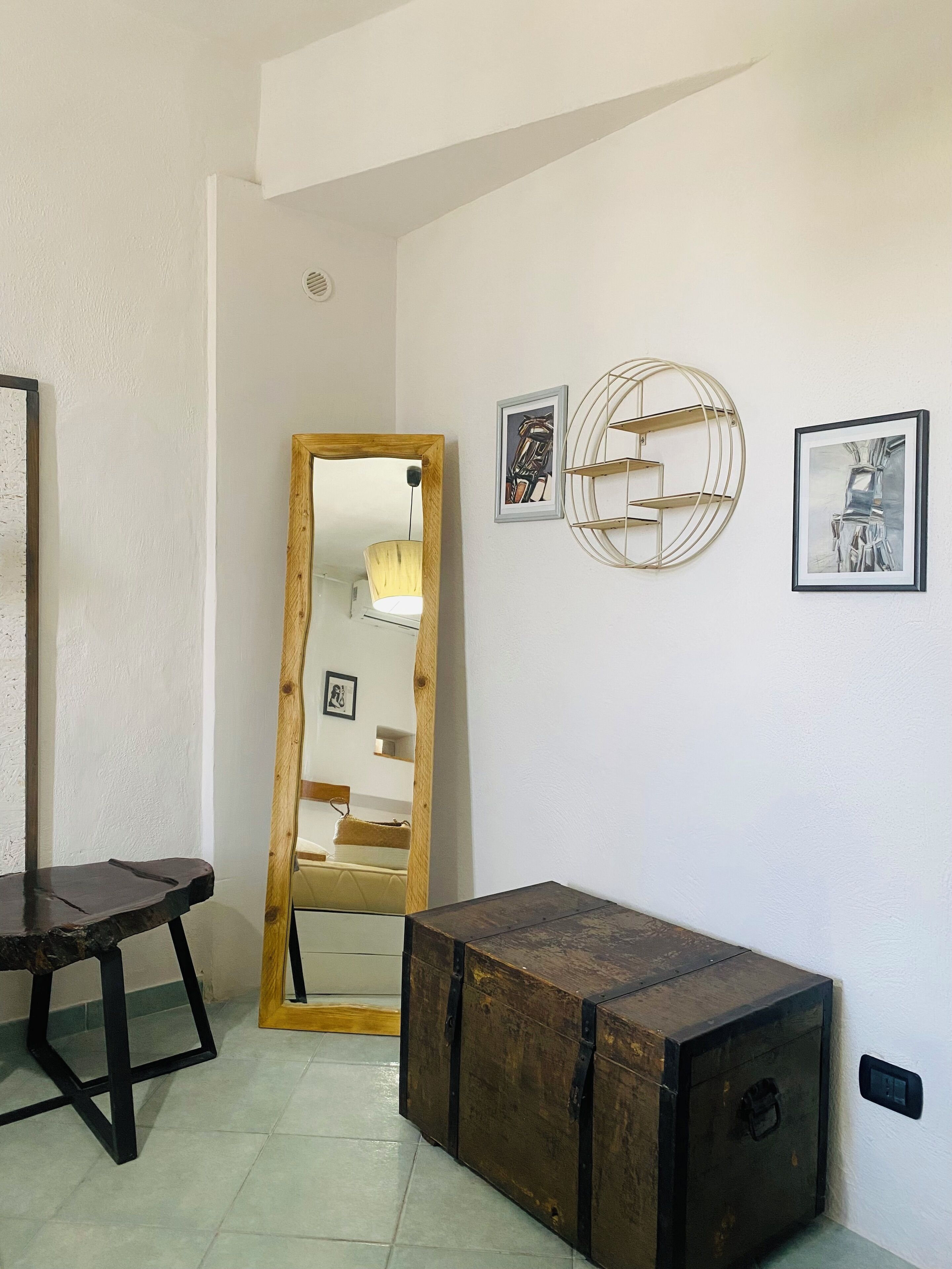 Una habitació amb un mirall gran, un cofre de fusta i dos quadres al mur.