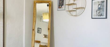 A room with a large mirror, a wooden chest, and two framed artworks on the wall.