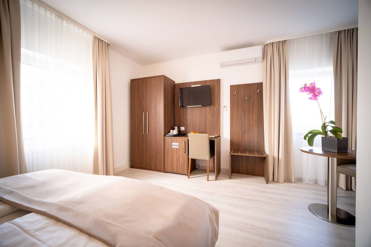 A hotel room with a bed, a desk, a TV, and a window with curtains.