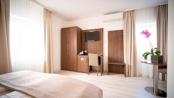 A hotel room with a bed, a desk, a TV, and a window with curtains.