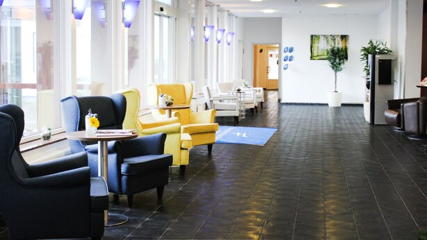 A hotel lobby with seating areas, a reception desk, and a large window. - Anor Hotel I Park Sleep & Fly I Frankfurt Airport (Moerfelden-Walldorf)