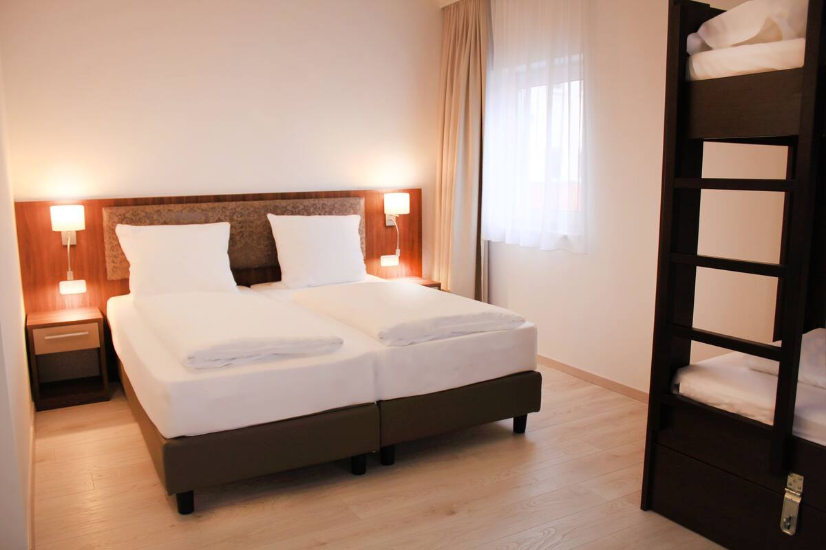 A double bed with two pillows, a wooden headboard, bedside lamps, and a wooden floor.