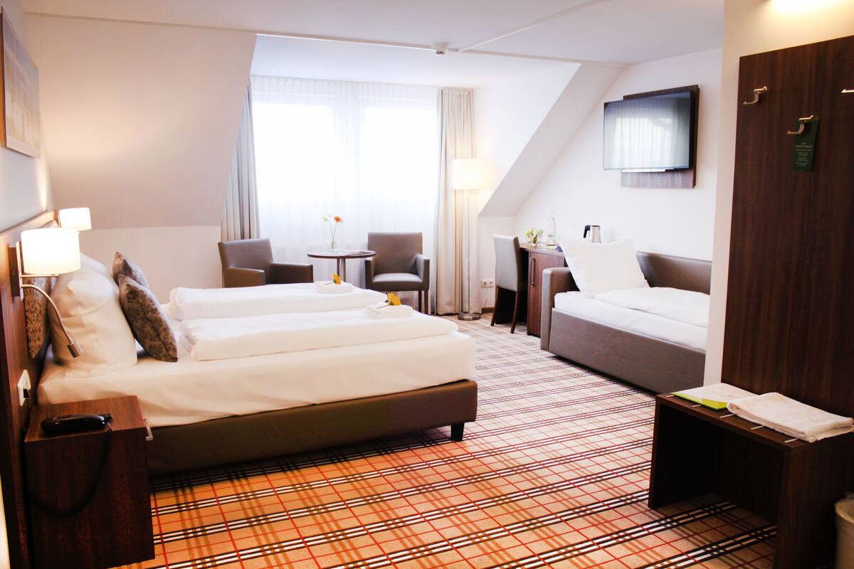 A hotel room with a bed, a sofa, a desk, and a TV.