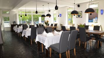 Un restaurante con varias mesas dispuestas para comer, amplios ventanales y lámparas colgantes.