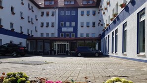 A courtyard with a car parked in front of a building with multiple windows and a sign. - Anor Hotel I Park Sleep & Fly I Frankfurt Airport (Moerfelden-Walldorf)