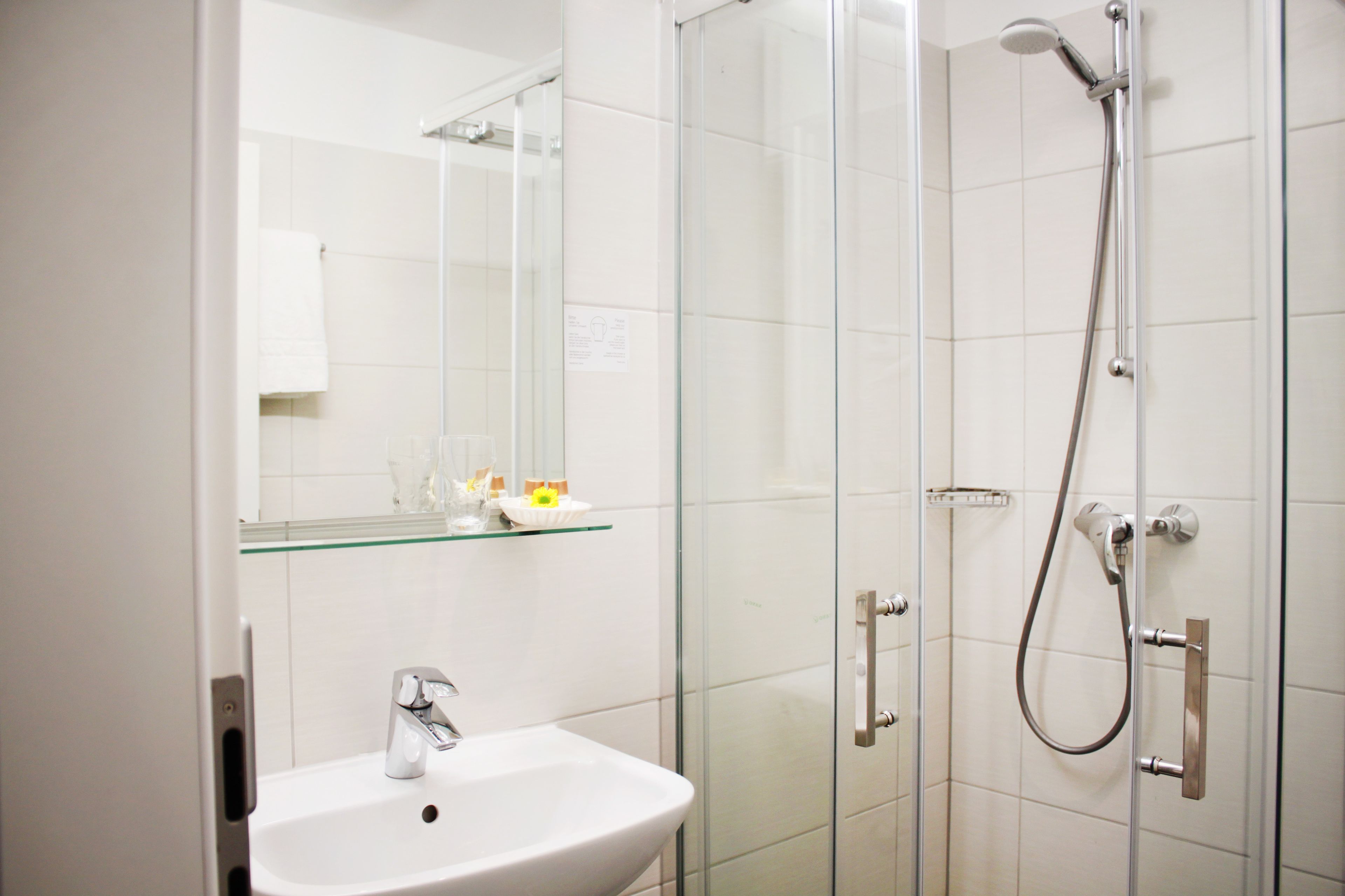 A modern bathroom with a glass shower enclosure, a white sink, and a glass shelf above the sink.