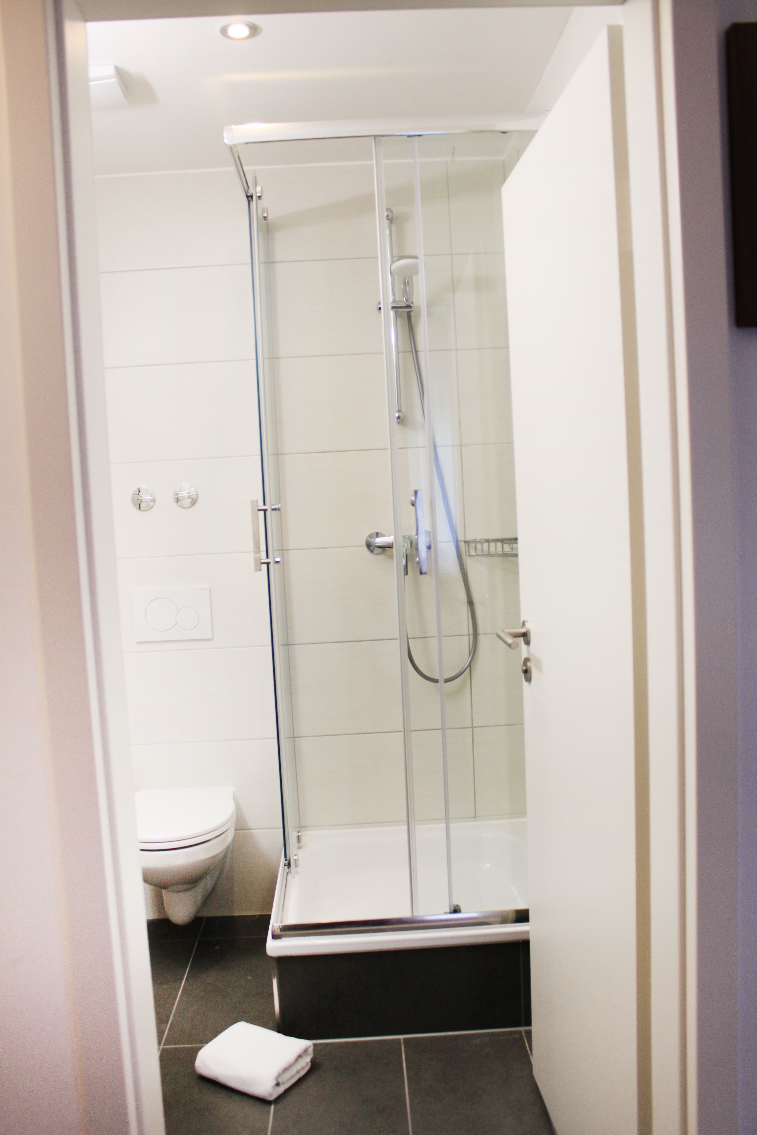 Une cabine de douche fermée par des parois en verre, avec des toilettes blanches et une serviette sur le sol.