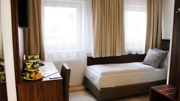 A hotel room with a bed, a desk with a chair, a TV, and a window with curtains.