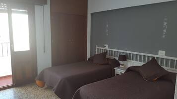 A room with two beds, a small table with a lamp, a chalkboard, and a door leading outside.