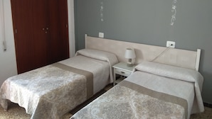 Una habitación de hotel con dos camas individuales, una mesita de noche con lámpara y un armario de madera.