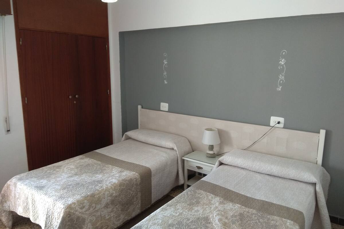 A hotel room with two single beds, a bedside table with a lamp, and a wooden wardrobe.