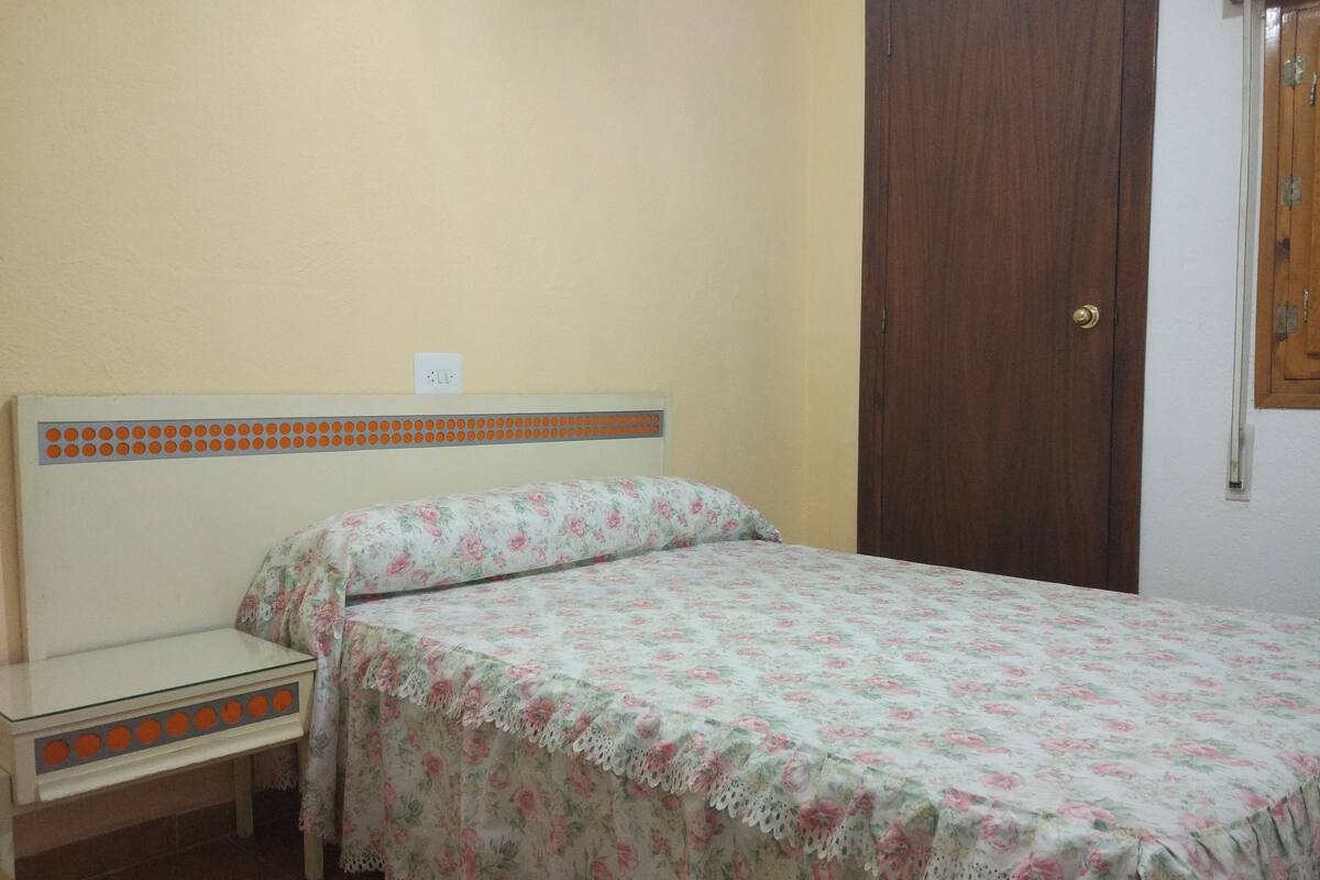 A bedroom with a single bed, a nightstand, a wooden door, and a wall socket.