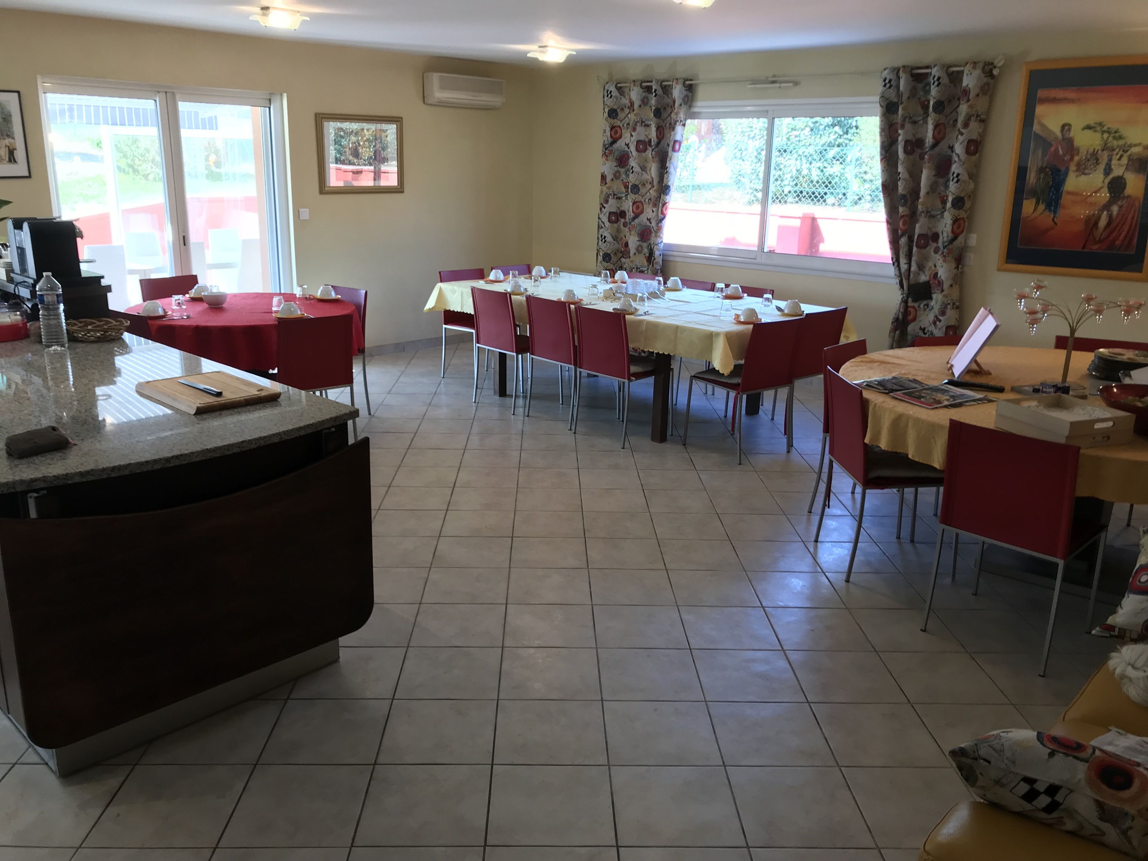 A dining area with multiple tables and chairs, a kitchen counter, and a window with curtains.