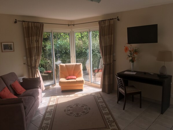 Una sala de estar con sofá, sillón, escritorio y ventanas amplias.