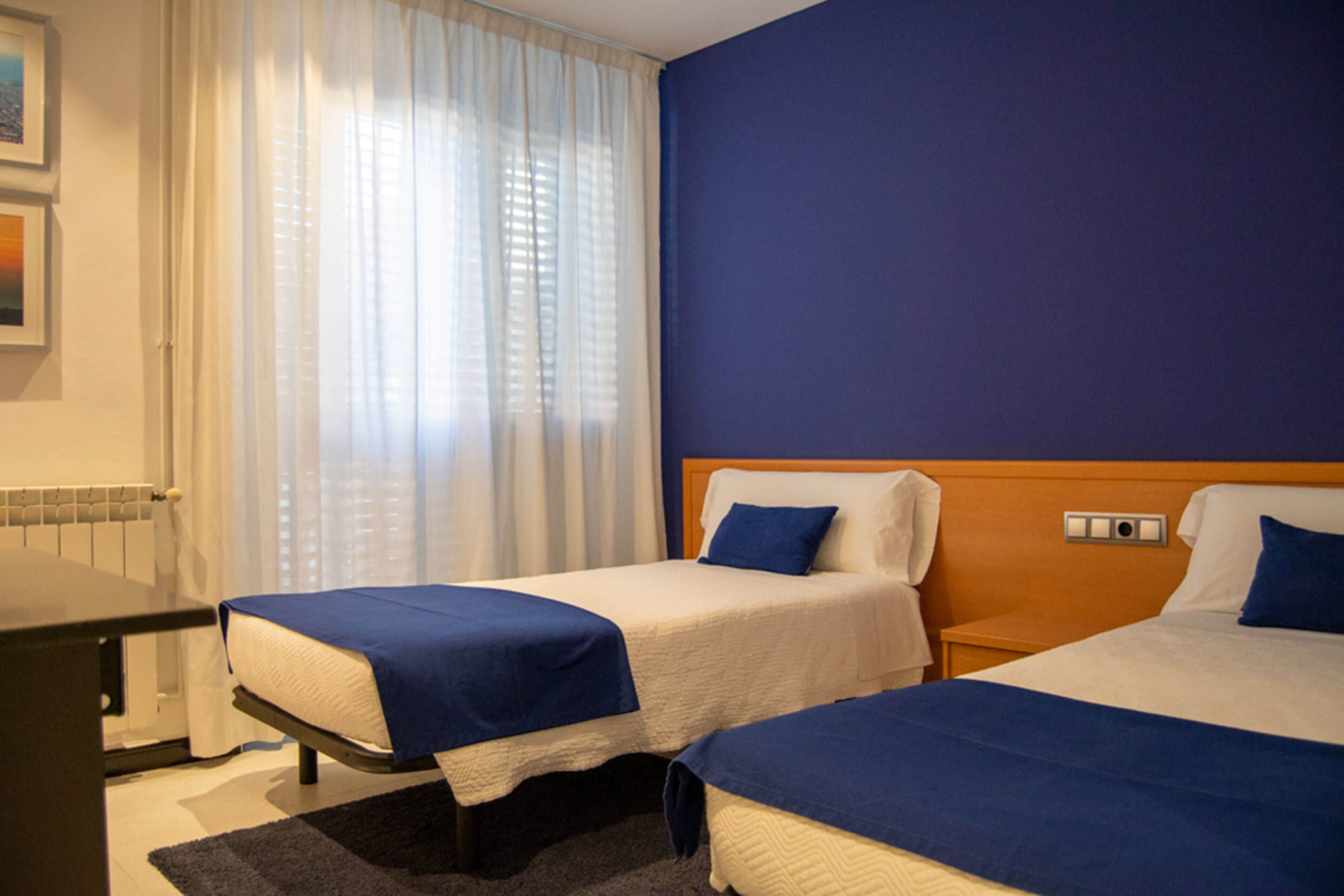 Une chambre d’hôtel avec deux lits, un bureau et une fenêtre avec des rideaux.