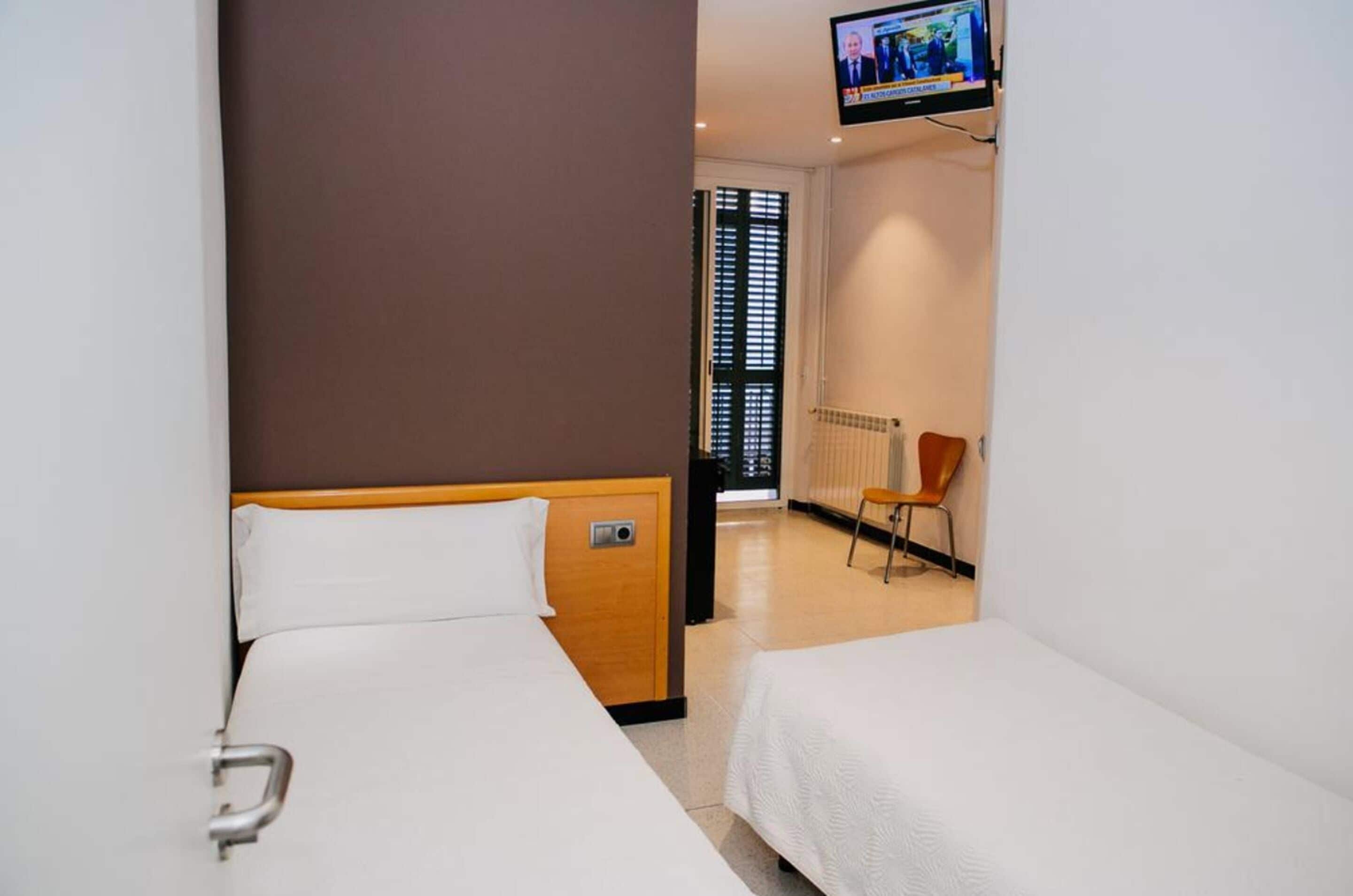 A hotel room with two single beds, a TV mounted on the wall, a radiator, and a chair.