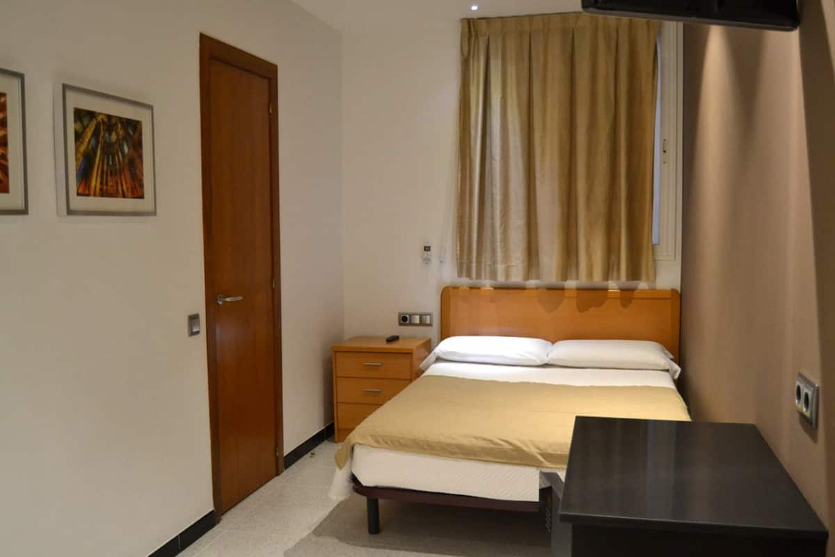 Una habitación de hotel con cama, mesita de noche y ventana con cortinas.