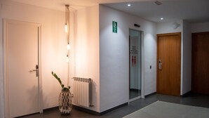 A hallway with a white door, a radiator, a plant, and a sign indicating the location of the bathrooms. - Hostal Apolo (Barcelona)