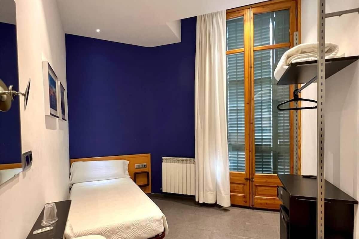 Habitación de hotel moderna con cama, mesita de noche con un vaso, lavabo, silla y radiador.