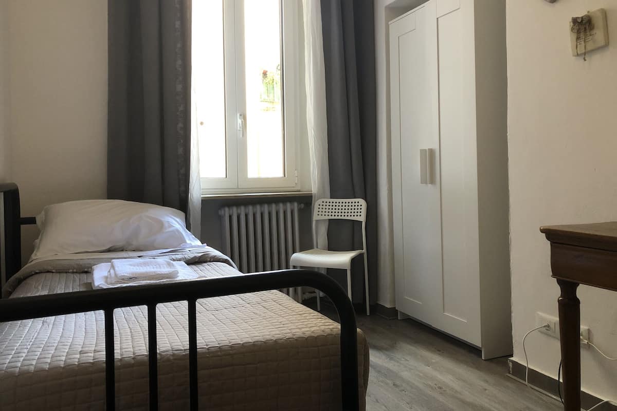 A bedroom with a bed, a chair, a wardrobe, and a window with curtains.