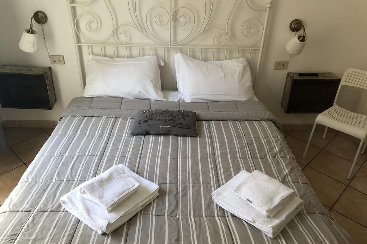 A neatly made bed with striped bedding and two pillows, a small table with a lamp, and a chair.