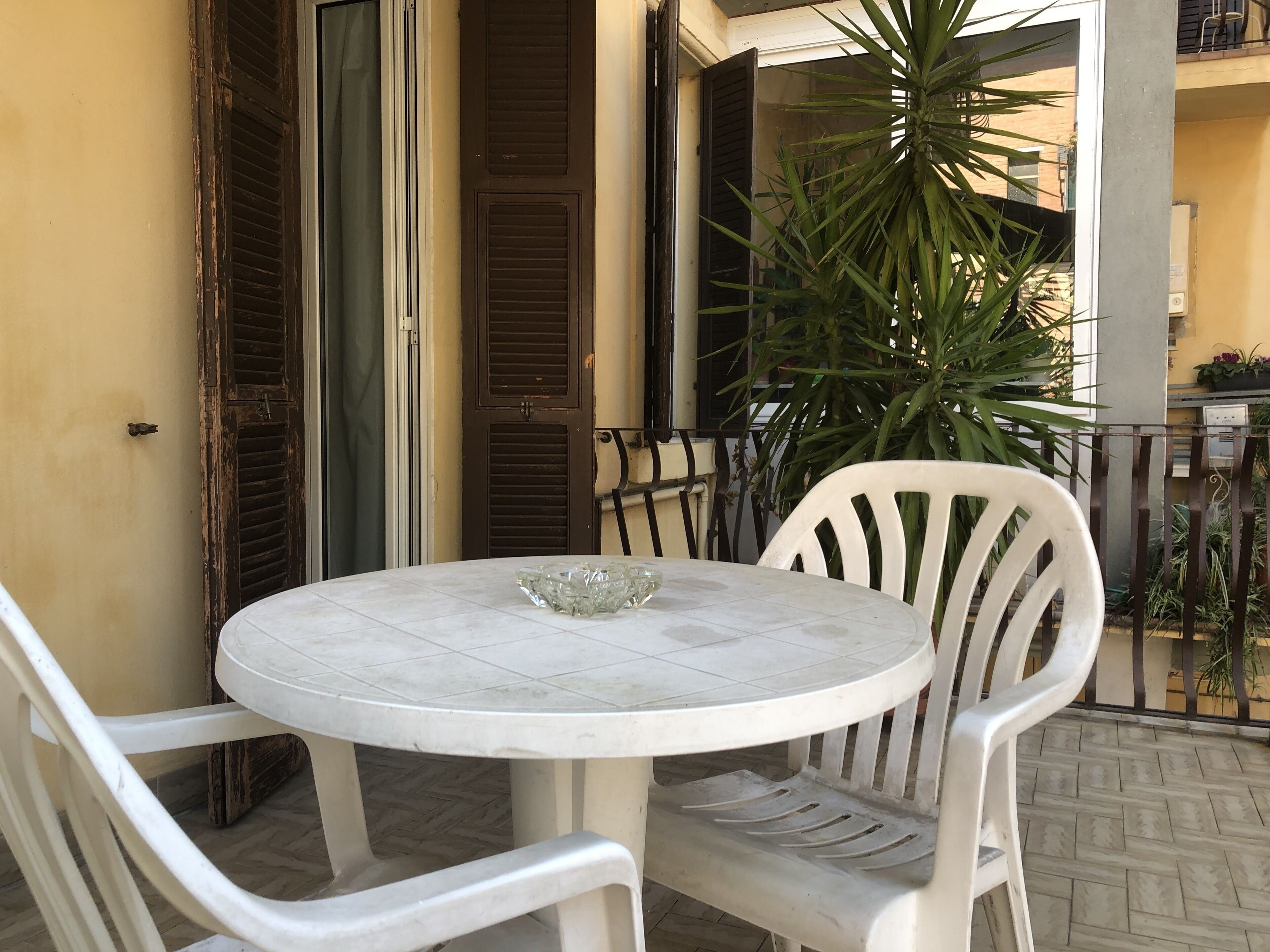 A round table with a glass bowl, two white plastic chairs, and a potted plant.