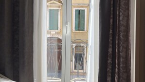 A room with a bed, a window with curtains, and a view of buildings outside. - Ai Leoni (Verona)