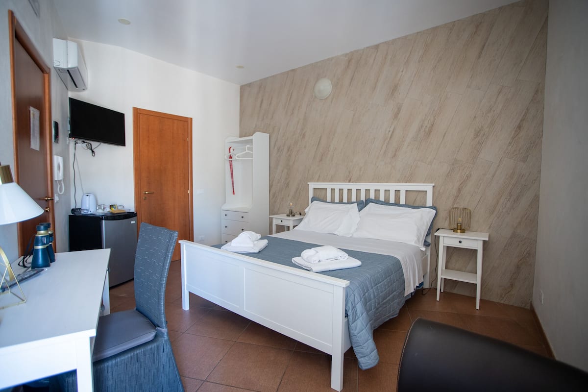 A bedroom with a bed, a desk, a chair, a wardrobe, and a television.